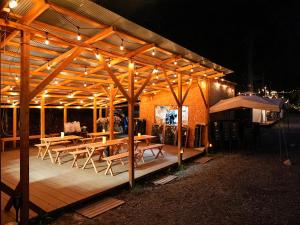 a wooden pergola with tables and chairs under it at night at リバーサイドグランピングNuts in Higashiomi