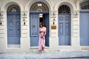 Una mujer con un vestido rosa parada frente a las puertas azules en Palazzo Ignazio, en La Valeta