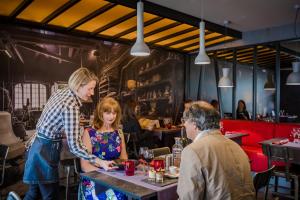 Ein Mann und eine Frau stehen an einem Tisch in einem Restaurant in der Unterkunft Logis Hôtel Restaurant Le Fruitier in Villedieu-les-Poëles