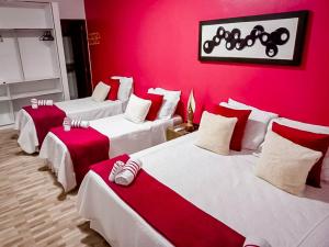 3 lits dans une chambre avec un mur rouge dans l'établissement Pousada Primavera, à São Miguel do Gostoso