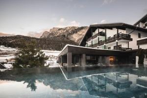 a hotel with a swimming pool in front of a mountain at Biancaneve Family Hotel in Selva di Val Gardena