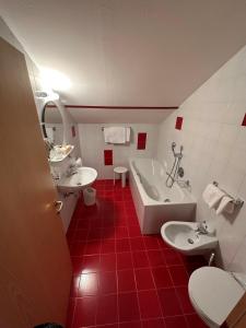 uma casa de banho vermelha e branca com 2 lavatórios e uma banheira em Hotel Brandl em San Candido