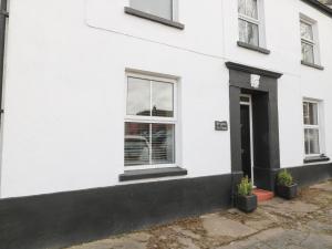 a white house with a black door and two potted plants at Bryants Cottage in Chulmleigh