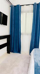 1 dormitorio con cortinas azules, 1 cama y TV en Sweet home, en Dakar