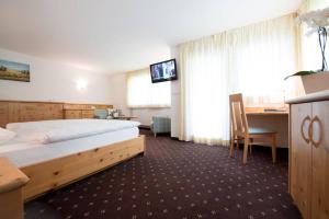 Cette chambre comprend un lit, un bureau et une télévision. dans l'établissement Hotel Pinei, à Ortisei