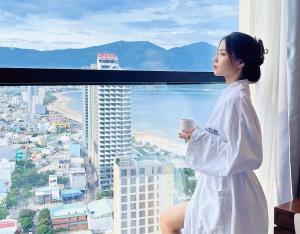 峴港的住宿－Luxury Apartment in Sheraton Building with Ocean View，坐在窗户上拿着咖啡的女人