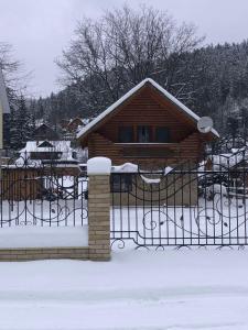 a log cabin with a fence in the snow at Yablunevyi Tsvit in Yaremche