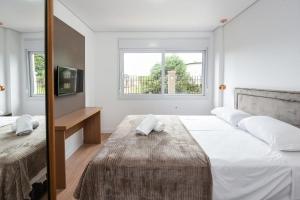 a white bedroom with a large bed and a mirror at Rosa Edifício Vivere Canela in Canela