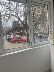 a window with a red car parked in a parking lot at L&M Apartment in Târgu-Mureş