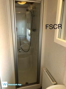 La salle de bains est pourvue d'une douche en verre et de toilettes. dans l'établissement First Steps Caravan Rentals, à Sandown