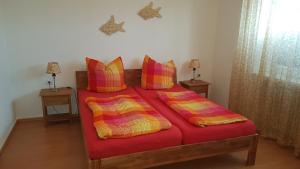 Schlafzimmer mit einem Bett mit roter Bettwäsche und bunten Kissen in der Unterkunft Ferienwohnungen Brasse in Dornumersiel + 37 Fotos