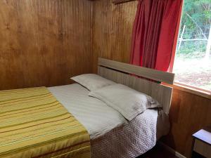 Ce lit se trouve dans une chambre en bois dotée d'une fenêtre. dans l'établissement Cabaña estero Huite, à Quemchi