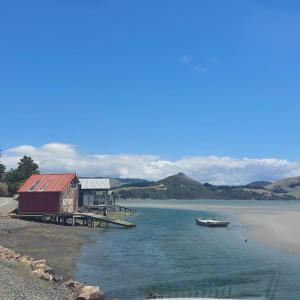 a house on the shore of a lake with a boat at Otago Peninsula Paradise in Dunedin +24 photos