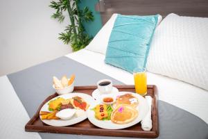 a tray of breakfast foods and a glass of orange juice on a bed at Kali Hotel in Santa Ana