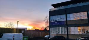 a building in a parking lot with a sunset in the background at London gateway studio flat in Borehamwood
