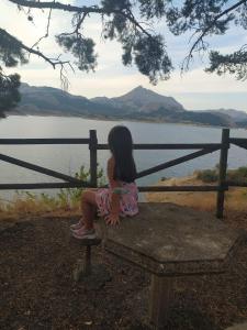 una niñita sentada en un banco mirando el agua en Los Tres Hórreos, en Felechas