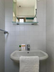 Baño blanco con lavabo y espejo en Pensione Ornella en Lignano Sabbiadoro