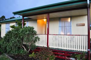 a small white house with a sign on it at GreenGate Cottages in Strahan