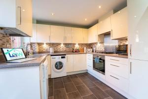 cocina con armarios blancos, lavadora y secadora en Brookfield, en Horley