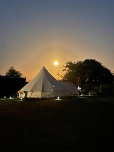 een witte tent in een veld met de zonsondergang op de achtergrond bij Cox Hill Glamping Benson in Truro