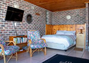 a bedroom with a bed and two chairs and a tv at Kormorant in Gansbaai