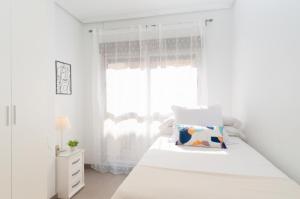a white bedroom with a bed and a window at Apartamentos Turisticos Rent Guardamar in Guardamar del Segura