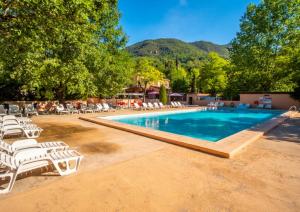 a swimming pool with white lounge chairs and trees at Camping Hotel Les Rives du Loup in Tourrettes-sur-Loup