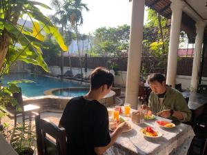 Dois homens sentados à mesa a comer à frente de uma piscina. em Lucky Private Boutique Pool Villa em Siem Reap
