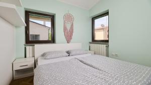a white bedroom with a bed and two windows at Apartment Iriska in Novigrad Istria