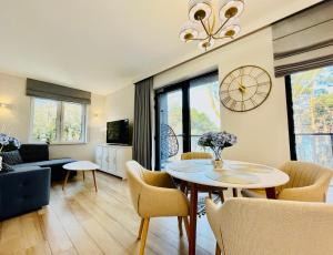 sala de estar con mesa, sillas y reloj en Baltic View Apartament - Dwie Sosny, en Ustronie Morskie