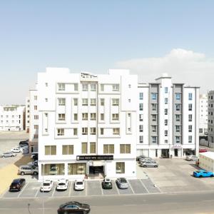 un edificio blanco con coches estacionados en un estacionamiento en Sama Muscat Hotel en Al Khawḑ