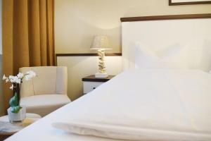 ein Schlafzimmer mit einem weißen Bett und einem Stuhl in der Unterkunft Hotel Strandschlösschen in Travemünde