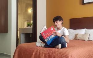 Posada Del Carmen Aguascalientes في اغواسكالينتيس: طفل صغير جالس على سرير يقرا كتاب