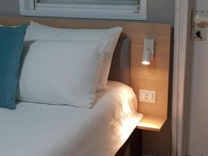 un letto con cuscino bianco e interruttore della luce di Airport Guest House a Or Yehuda