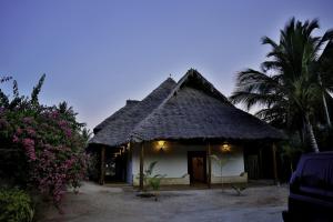 a hut with a thatched roof and palm trees at Tamani Villas in Matemwe