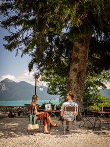 mężczyzna i kobieta siedzący na krześle pod drzewem w obiekcie Wallerei Walchensee w mieście Walchensee