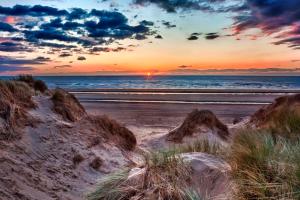 a sunset on a beach with the ocean and sand at Dora Cottage in Formby