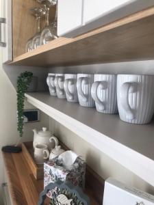 een rij witte vazen op planken in een keuken bij The Cockle Shell Caravan, Seaview Holiday Park, Whitstable in Whitstable