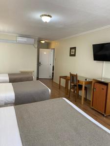 um quarto de hotel com duas camas e uma mesa e uma televisão em Hotel Melillanca em Valdivia