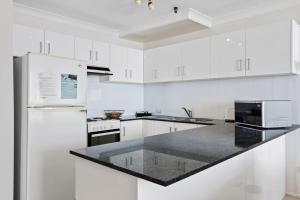 a white kitchen with white cabinets and a black counter top at Focus Apartments With Ocean Views in Gold Coast