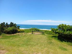 a bench sitting on the grass near the ocean at Suítes a Beira Mar in Rio das Ostras