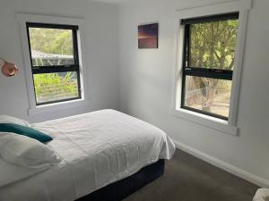 a white bedroom with a bed and two windows at Little White House on Ecclestone, Riverside in Alanvale