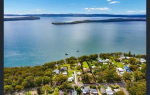 an aerial view of a lake with houses and a boat at A LAKEHOUSE ESCAPE - a Waterfront Reserve on shores of Lake Macquarie in Bonnells Bay