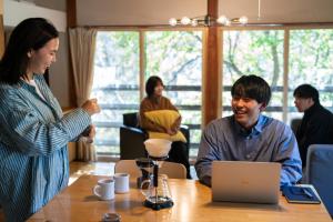 een vrouw die praat met een man aan een tafel met een laptop bij NORTHSTAR Loft in Matsumoto