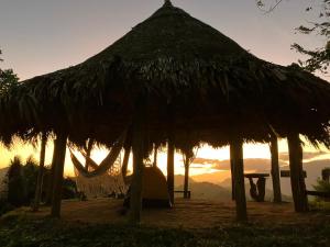 a straw hut with a tent and a sunset in the background at La Cima Tayrona in Santa Marta