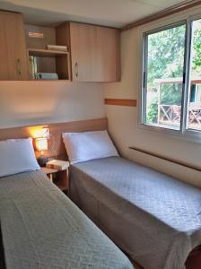 2 Betten in einem kleinen Zimmer mit Fenster in der Unterkunft Villaggio Turistico Il Lago Dorato in Carlazzo