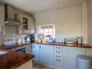 uma cozinha com armários brancos e uma bancada em Thimble Cottage em Lower Slaughter