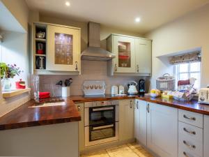 uma cozinha com armários brancos e um forno com placa de fogão em Thimble Cottage em Lower Slaughter