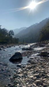 a river with rocks and the sun in the sky at Hedony Farmhouse with 2 Bedrooms and Swimming pool in Rishīkesh