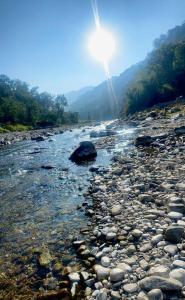a river with rocks and the sun in the background at Hedony Farmhouse with 2 Bedrooms and Swimming pool in Rishīkesh